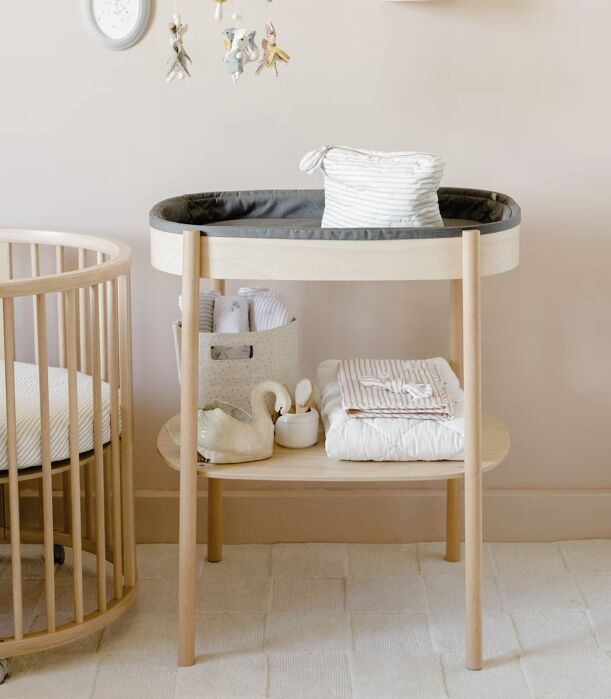 A round wooden baby changing table with storage shelves, positioned next to a matching round crib.