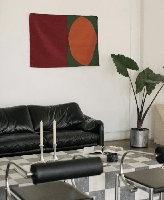 A bold red, green, and orange geometric textile hangs on the wall of a styled room. 