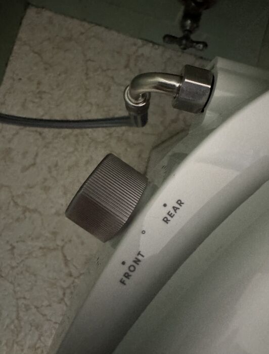 A close-up of a control knob labeled “Front” and “Rear” on a white appliance, with a metal hose connected above it.