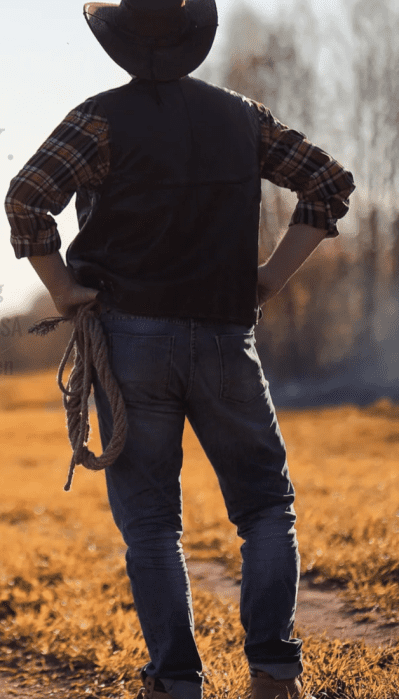 A man in American-made jeans standing in a field holding a loop of rope. 