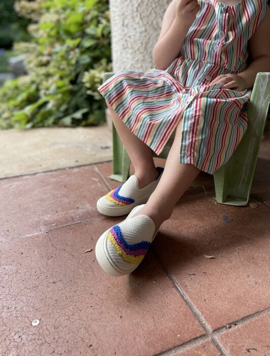 A little girl lounging in a tiny chair wearing Rothys. 
