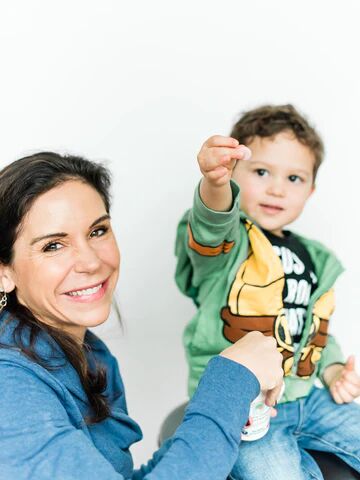 A child seated next to their parent, holding up Raise Them Well chewable multivitamins.