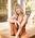 Blonde woman in rust-colored workout set smiles while sitting on a deck