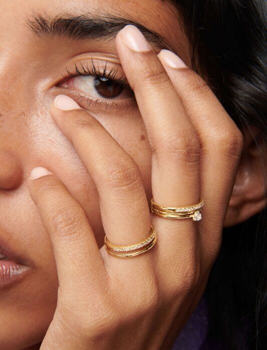 Close-up of a woman touching her face with her fingers adorned with elegant gold rings, highlighting her manicured nails and detailed facial features.