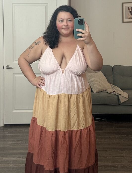 Woman in a multi-colored maxi dress taking a selfie with her phone in a mirror.