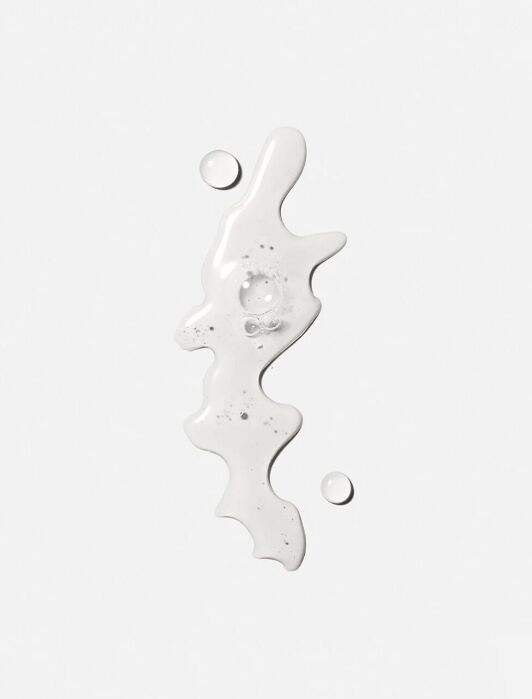 A white, liquid substance with a wavy shape and tiny bubbles is surrounded by two small droplets against a plain white background.