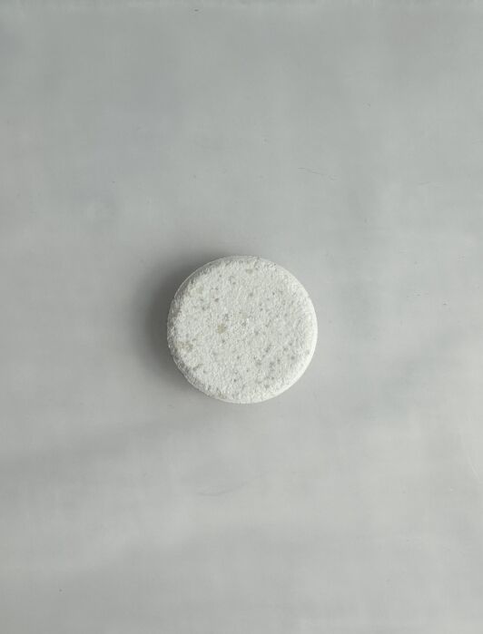 A round white tablet sits on a smooth, light gray surface.