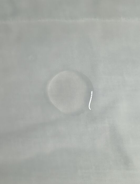 A small, circular wet spot is on a light grey surface.