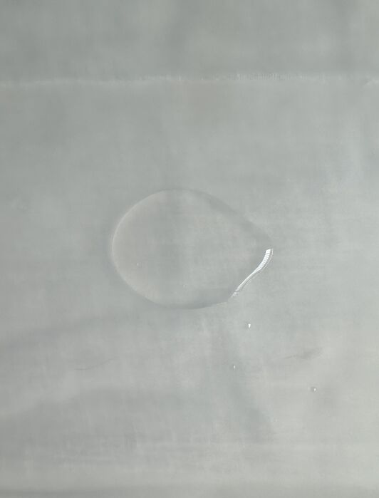 A single drop of clear liquid on a smooth, light-colored surface.