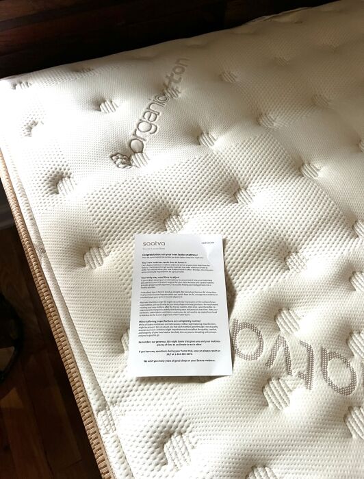 A new Saatva mattress is in the background labeled "Organic Cotton" and in the foreground are instructions and information for setting up a new Saatva mattress.