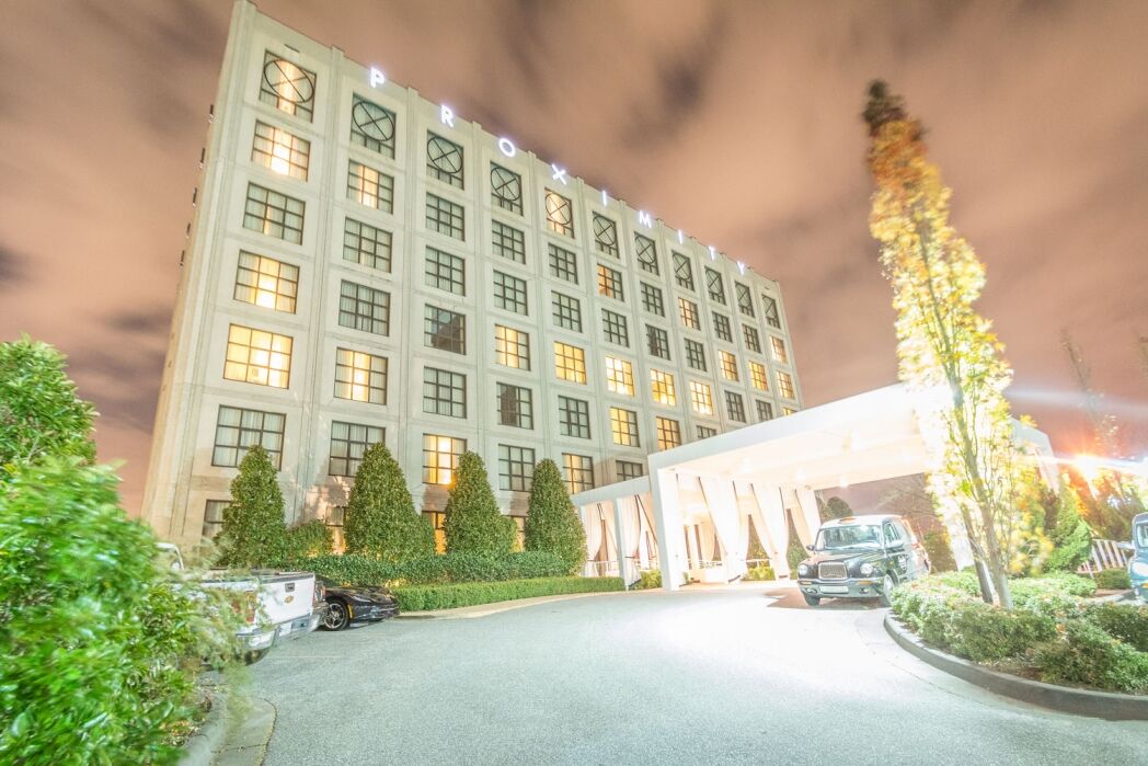 A multi-story hotel building with illuminated windows and a covered entrance, surrounded by trees and parked cars at night.