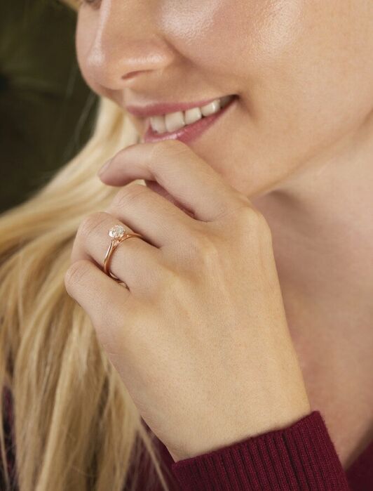 A woman with long blonde hair is smiling, wearing a large dangling earring and a gold ring with a gemstone on her finger.