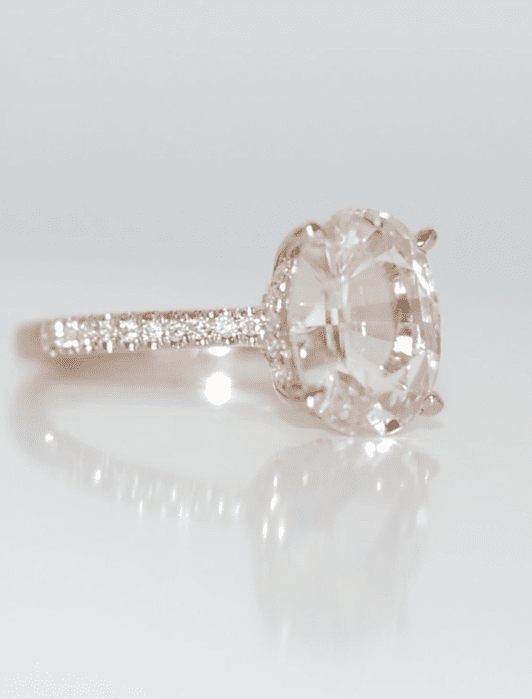 A rose gold ring with a large oval diamond at the center and a band adorned with small round diamonds.