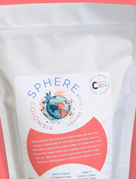 A white coffee bag labeled "Sphere Colombia Coffee Club" with descriptive text, set against a coral background.