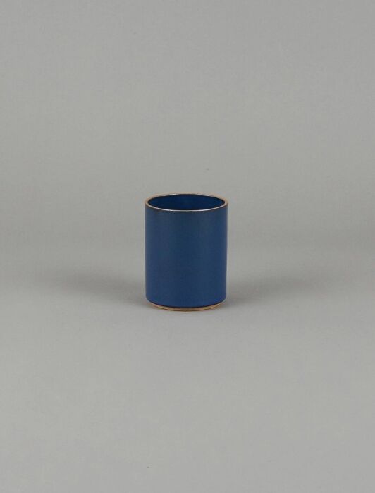A small, cylindrical blue ceramic cup with a smooth surface, placed on a plain gray background.