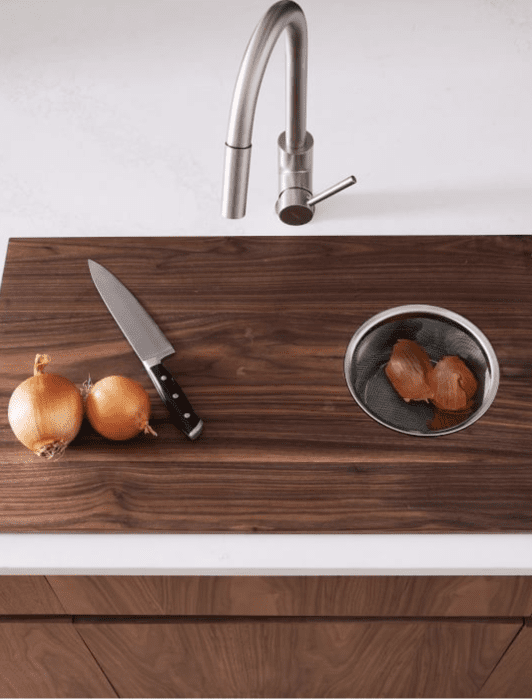 A kitchen countertop with two onions and a knife on the left, a sink with onion peels in a strainer on the right, and a modern faucet above.