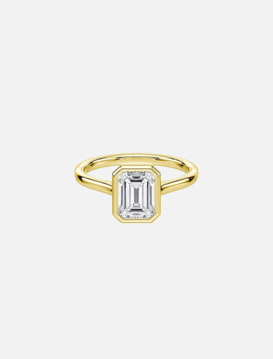 Gold ring with an emerald-cut diamond in a bezel setting on a plain band.