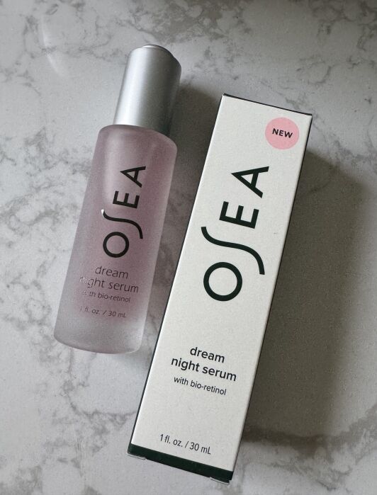 A bottle of OSEA Dream Night Serum with bio-retinol is placed next to its box on a marble surface. The box has a pink "NEW" label.