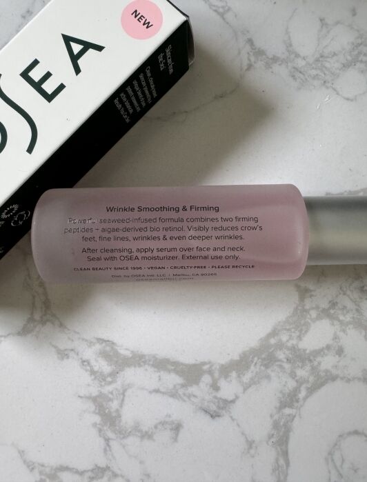 A pink bottle labeled "Wrinkle Smoothing & Firming" serum lies on a marble surface next to a partially visible OSEA product box.
