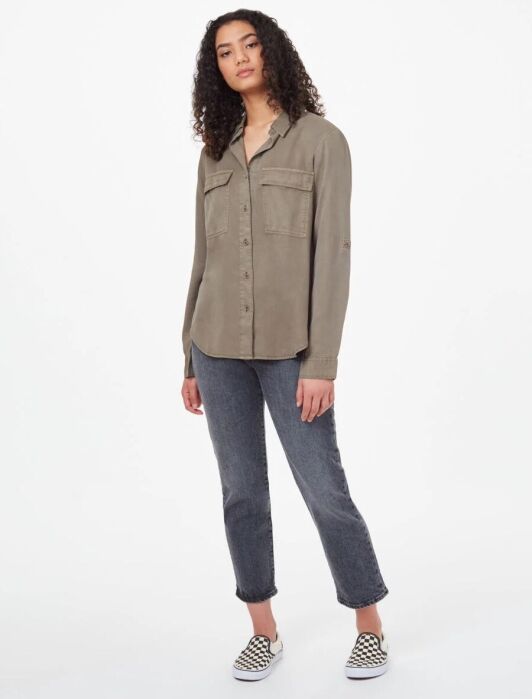 Person wearing a khaki button-up shirt, gray jeans, and checkered shoes, standing against a plain white background.