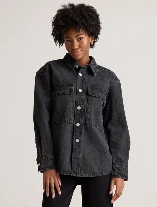 Person wearing a dark denim jacket with snap buttons, standing against a plain background.