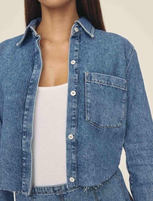 Person wearing a cropped denim jacket over a white ribbed tank top and high-waisted denim jeans.