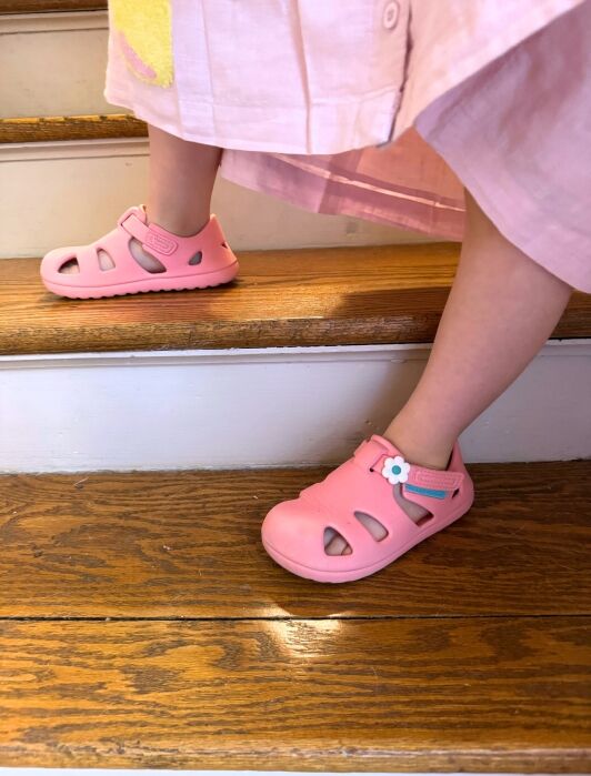 A child wearing a pink dress and pink sandals is stepping up wooden stairs.