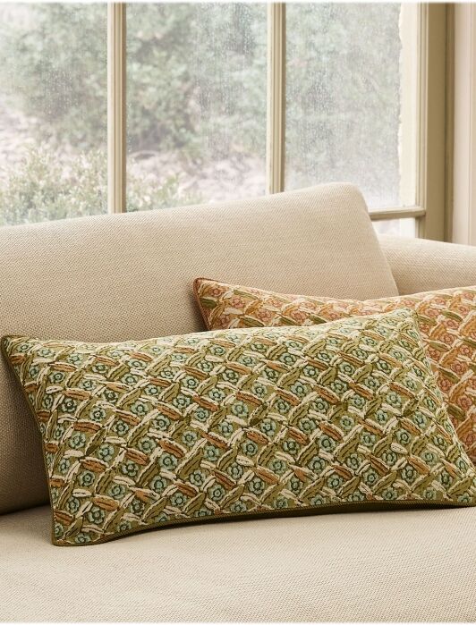 Two patterned rectangular pillows, one green and one orange, are placed on a light beige sofa in front of a window.