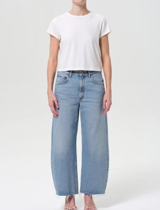 A person wearing a plain white short-sleeve crop top, light blue wide-leg jeans with frayed hems, and open-toe sandals stands against a white background.