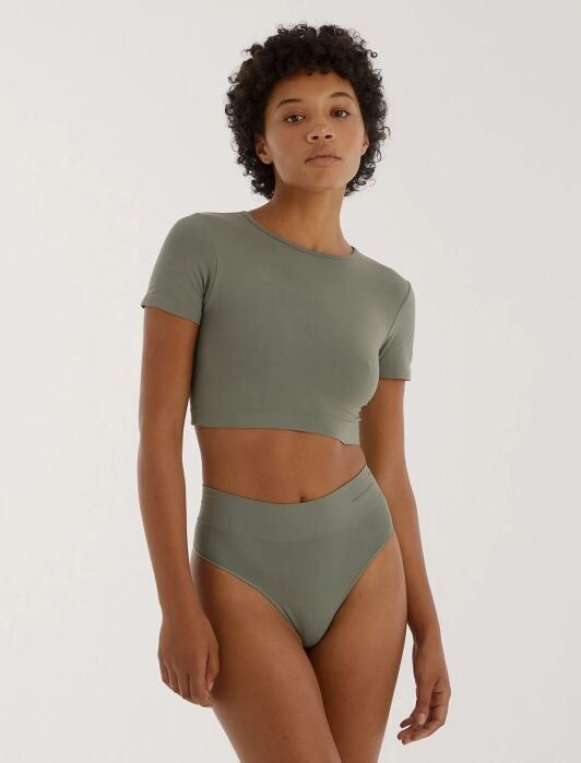 A woman stands against a neutral background wearing a sage green short-sleeve crop top and matching high-waisted underwear.