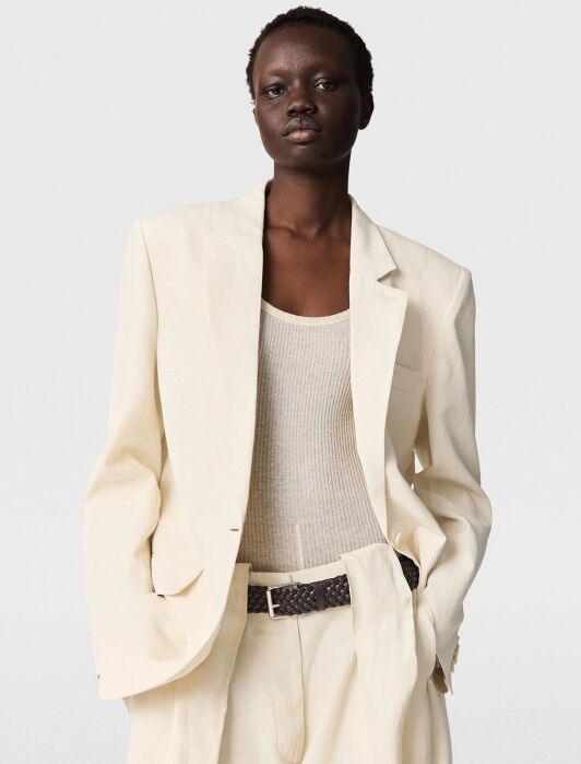 Person wearing a cream-colored suit with a matching tank top and a dark braided belt, posing against a plain light background.