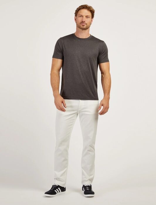 A man stands facing forward wearing a dark gray t-shirt, white pants, and black sneakers against a plain light background.