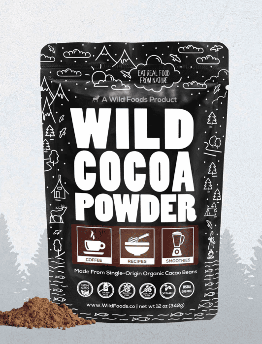 A black pouch labeled "Wild Cocoa Powder" with icons for coffee, recipes, and smoothies; a small pile of cocoa powder sits in front of the bag.