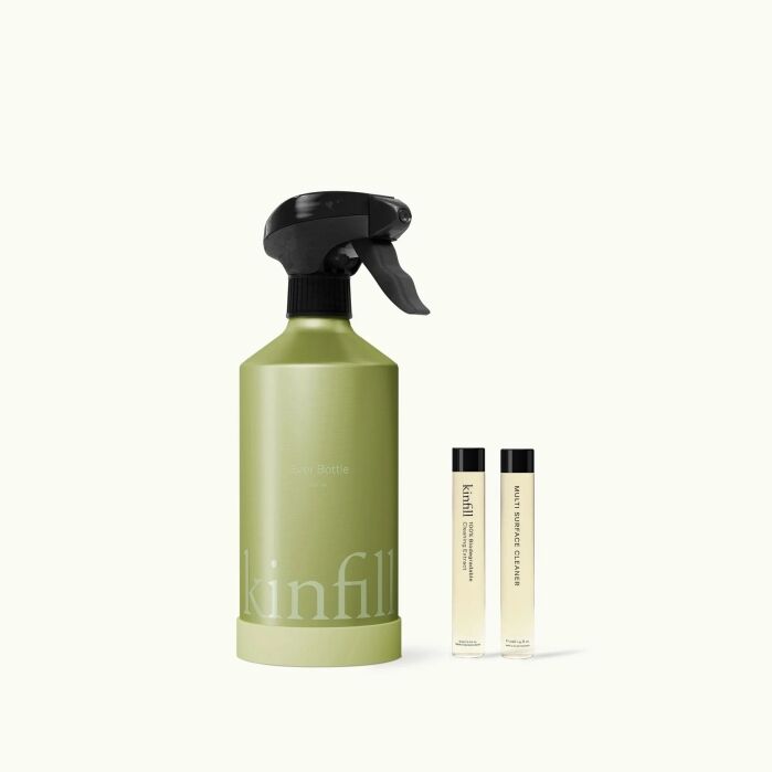 A green spray bottle labeled "kinfill" stands next to two small refill tubes with white labels on a plain light background.