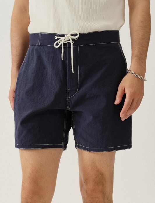 A person wearing navy blue drawstring shorts with white stitching and a white tank top, standing against a plain background.
