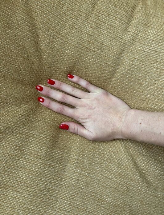 A hand with red nail polish is pressing down on a textured beige cushion.