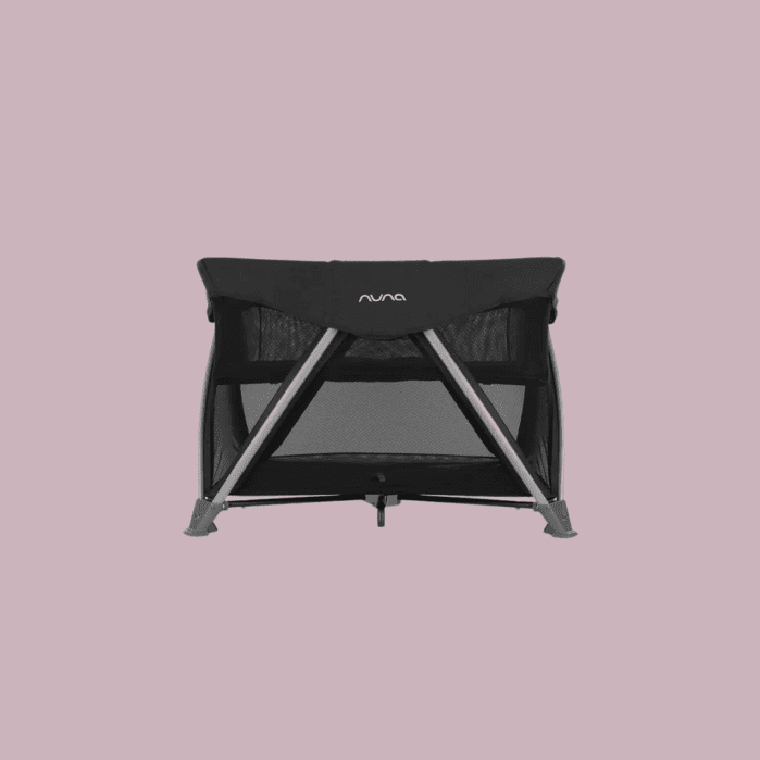 A black Nuna travel crib with mesh sides and a metal frame, shown against a plain light mauve background.