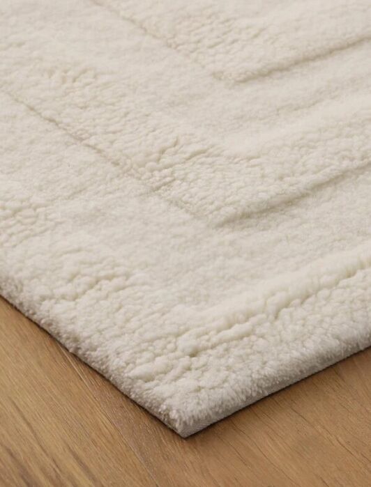 A close-up of a cream-colored, textured area rug with a raised pattern, placed on a wooden floor.