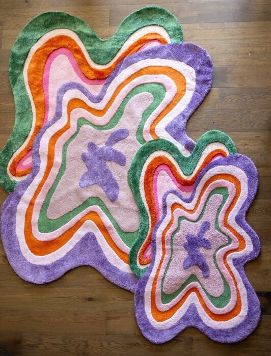Two irregularly shaped, colorful rugs with wavy patterns in shades of purple, pink, orange, and green are placed on a wooden floor.