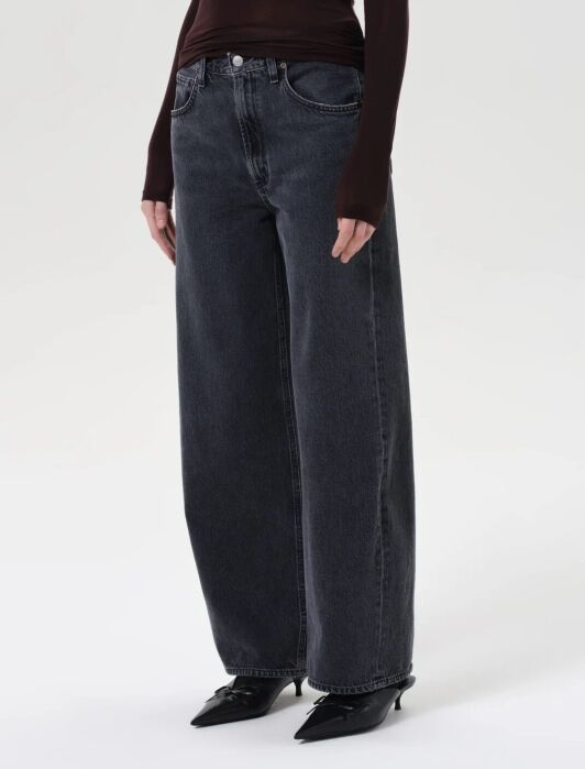 Person wearing wide-leg, faded black jeans with a high waist and black pointed-toe shoes, standing against a plain light background.