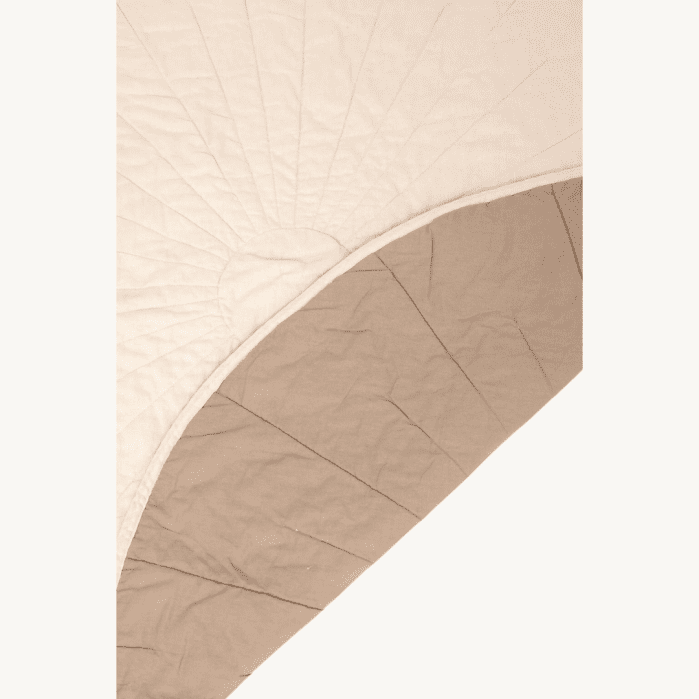 A close-up of a quilt with a sunburst stitching pattern on one side and a solid beige underside, partially folded over to show both sides.