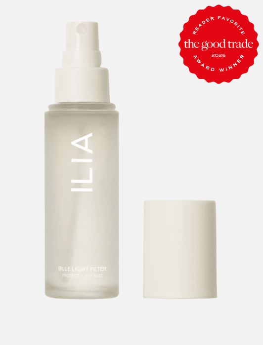 A clear bottle of ILIA Blue Light Filter Protect + Set Mist with a white cap removed, next to a red "The Good Trade Award Winner 2026" badge.