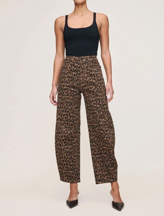 A person wearing a black tank top, high-waisted leopard print pants, and black pointed-toe heels stands against a plain background.