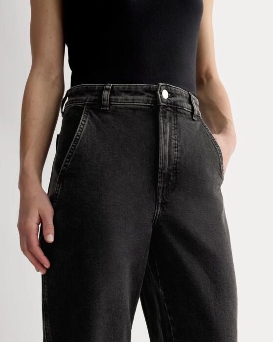 A person wearing a sleeveless black top and high-waisted, loose-fitting black jeans stands with hands in pockets.