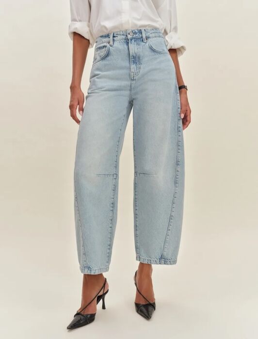 Person wearing light-wash, wide-leg jeans and a white shirt, paired with black pointed-toe heels, photographed against a plain background.