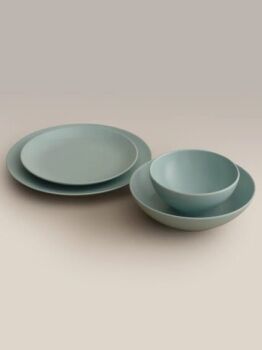 A set of matte light blue dishware including two plates, one bowl, and one shallow bowl, arranged on a neutral background.