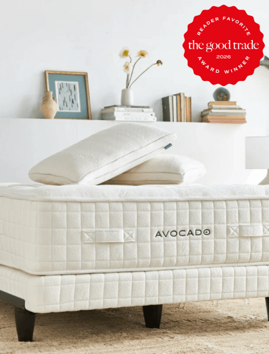 A neatly made Avocado mattress with pillows is shown in a bright, minimalist bedroom. A "Reader Favorite" award badge from The Good Trade is displayed in the top right corner.