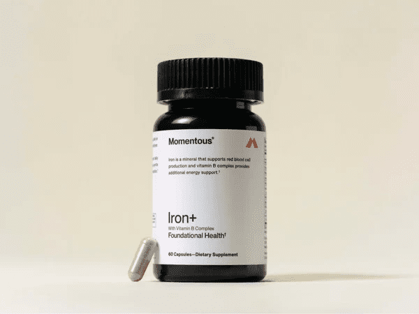 A bottle of Momentous Iron+ dietary supplement capsules with one capsule placed beside it on a plain background.