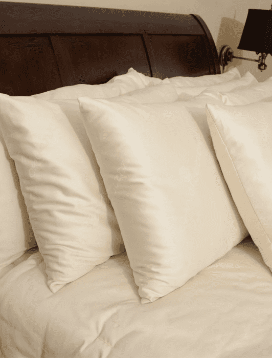 Four white pillows are neatly arranged against the dark wooden headboard of a bed with a cream-colored comforter.