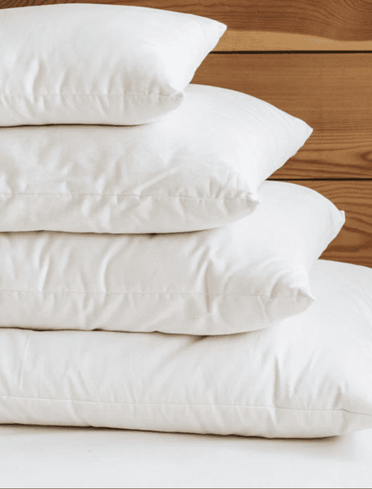 Four white pillows stacked on top of each other in front of a wooden background.